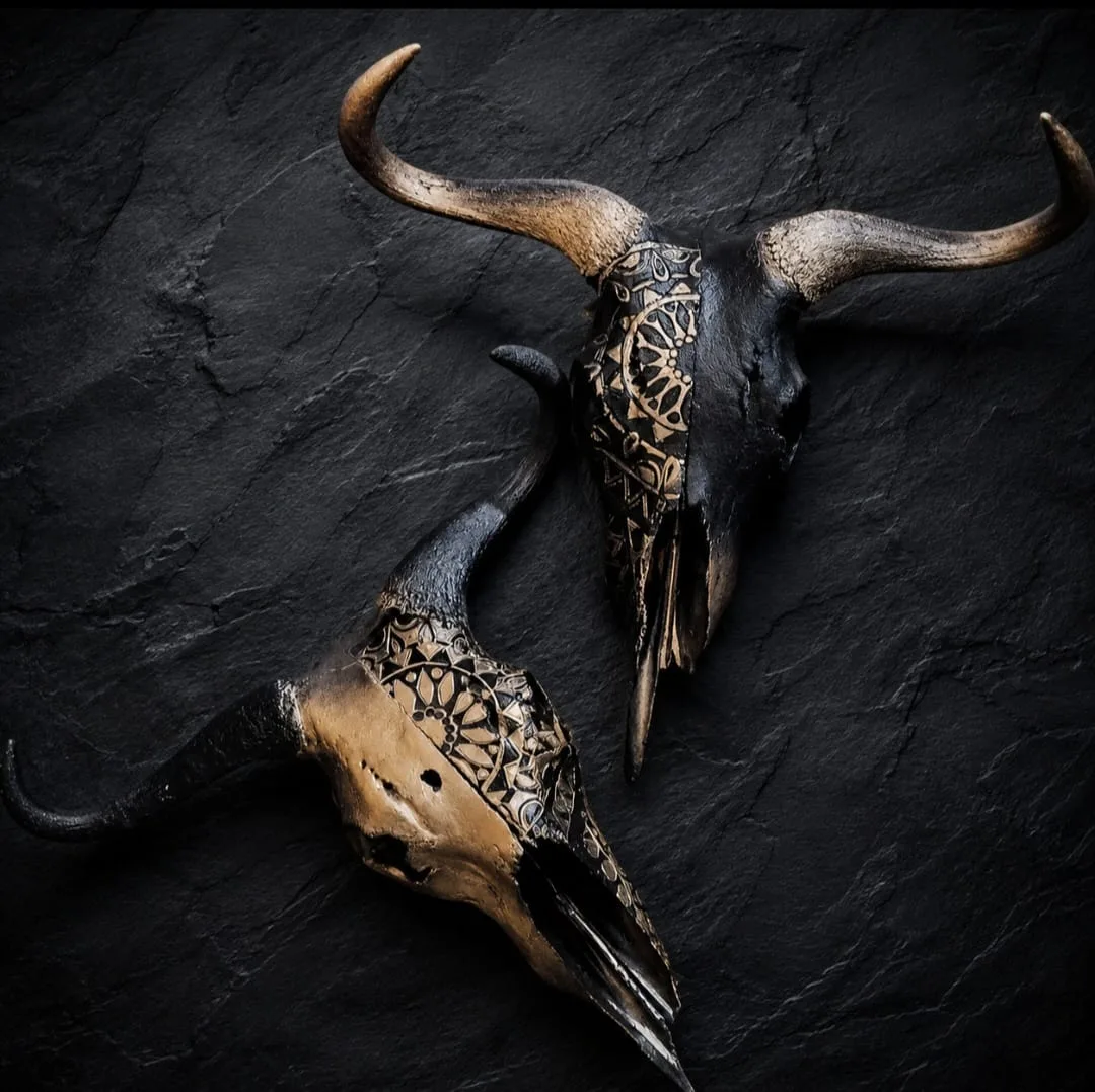 Two blue wildebeest skulls in copper and black, each carved with a half mandala pattern
