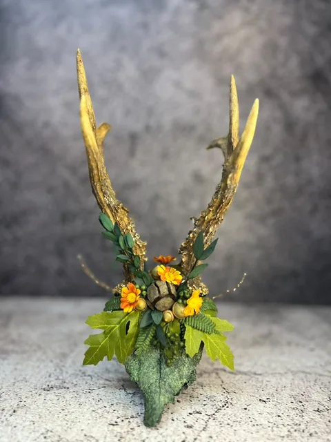 Antlered skull finished in moss-green texture and dressed with foliage and orange flowers